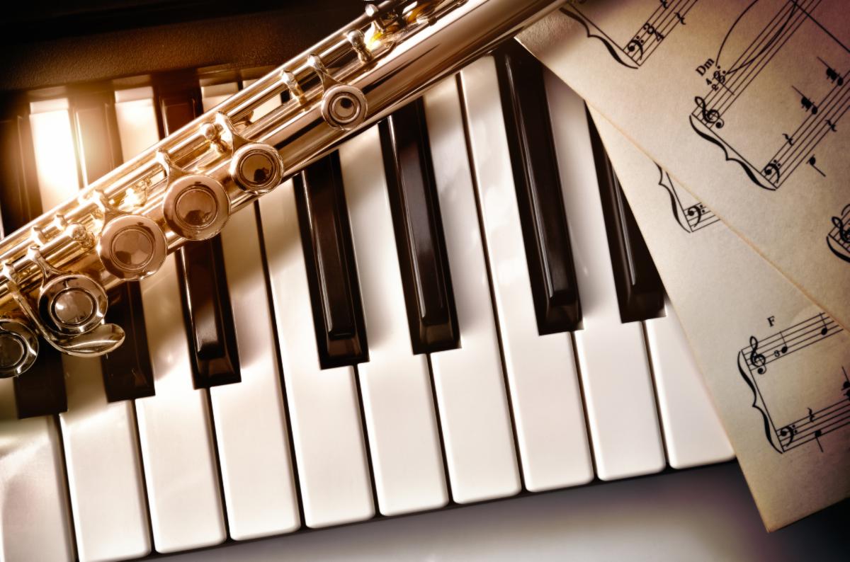 Closeup of flute laying over a piano and sheet music