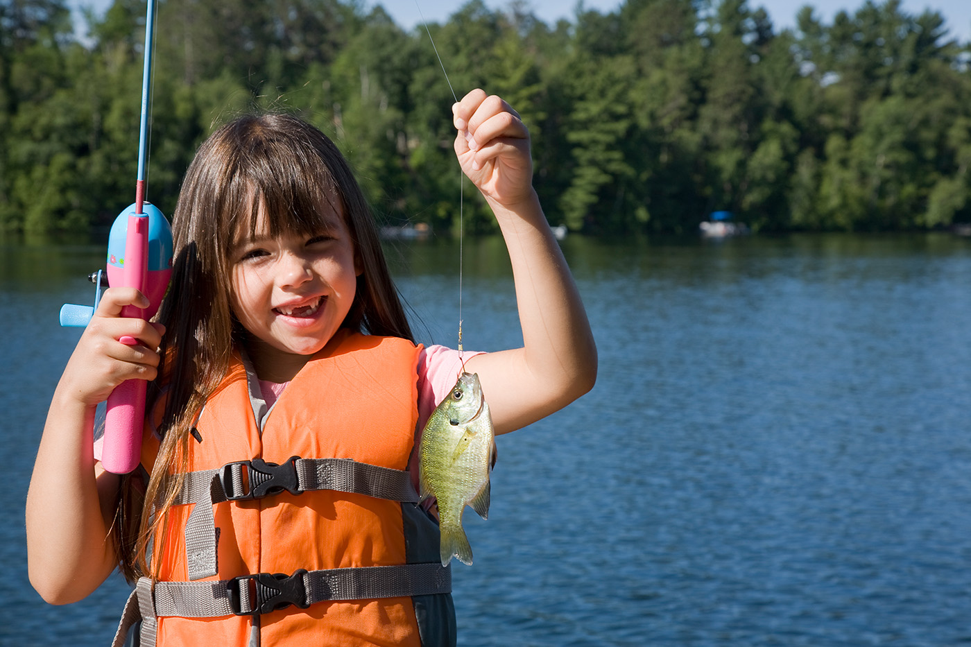 little girl in life vest holding up fish