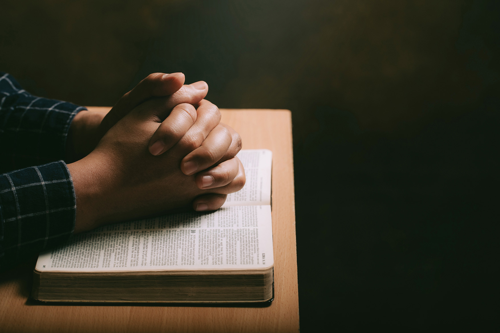 Hands folded in prayer on top of book
