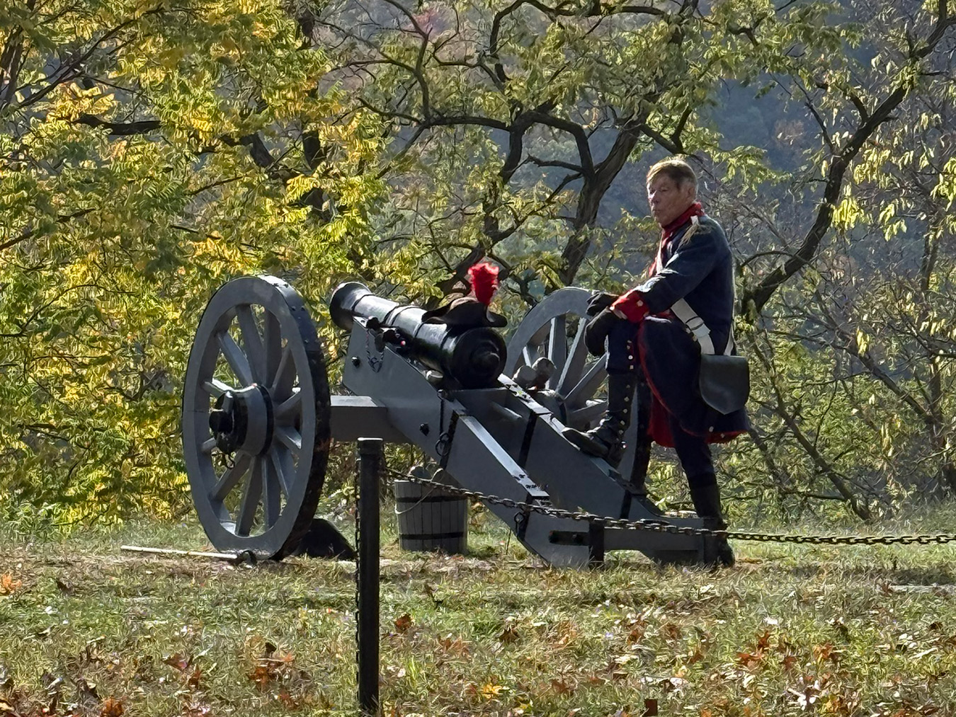 Man in Revolutionary War attire standing next to old-style cannon.