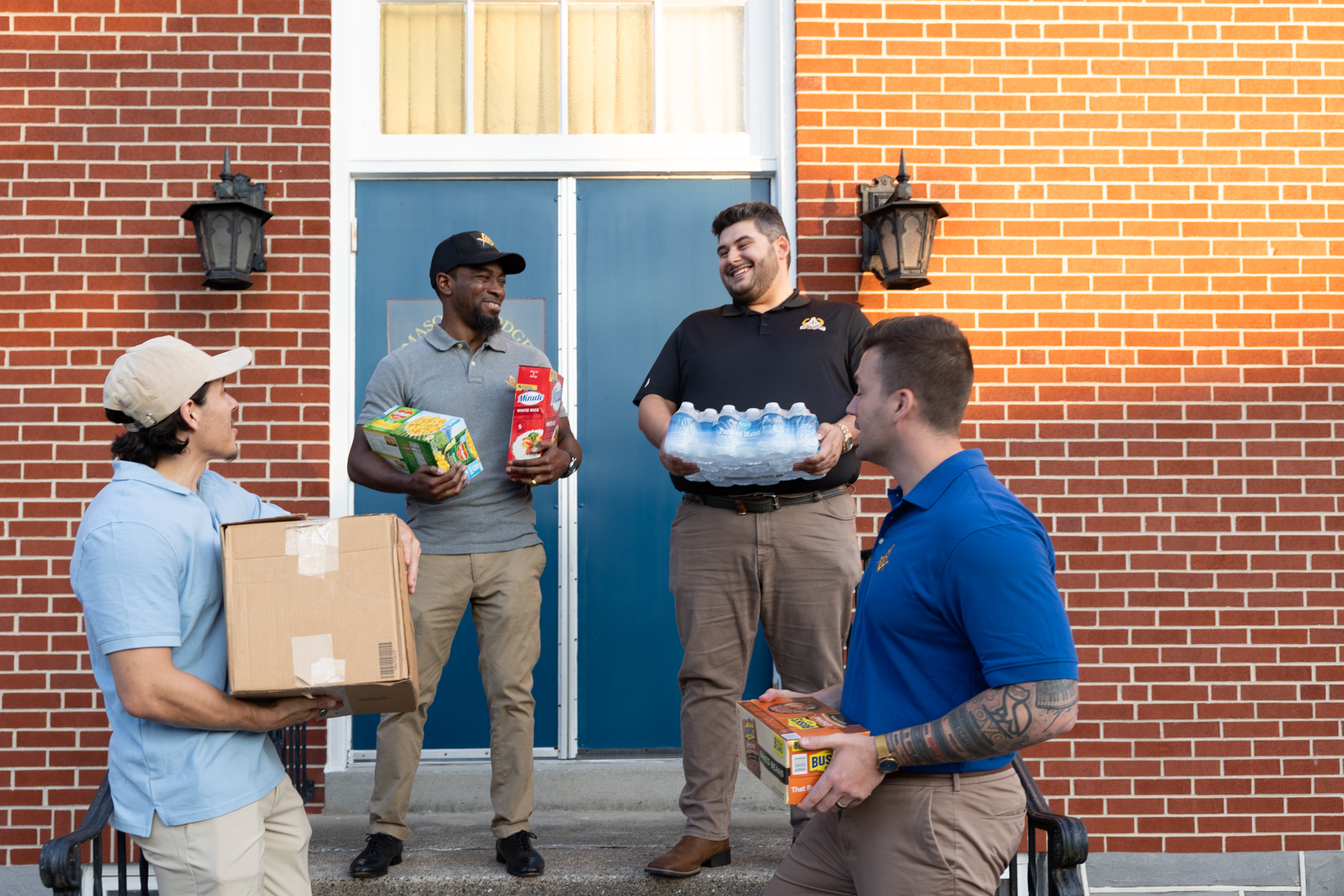 1W8A9348 Four young men standing in front of lodge while holding donations.